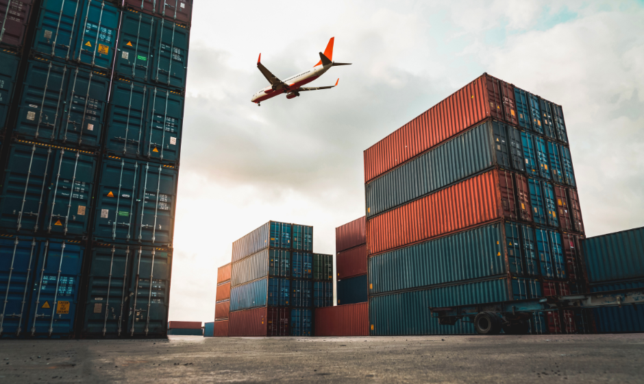 A plane flies over a yard of stacked shipping containers at a port