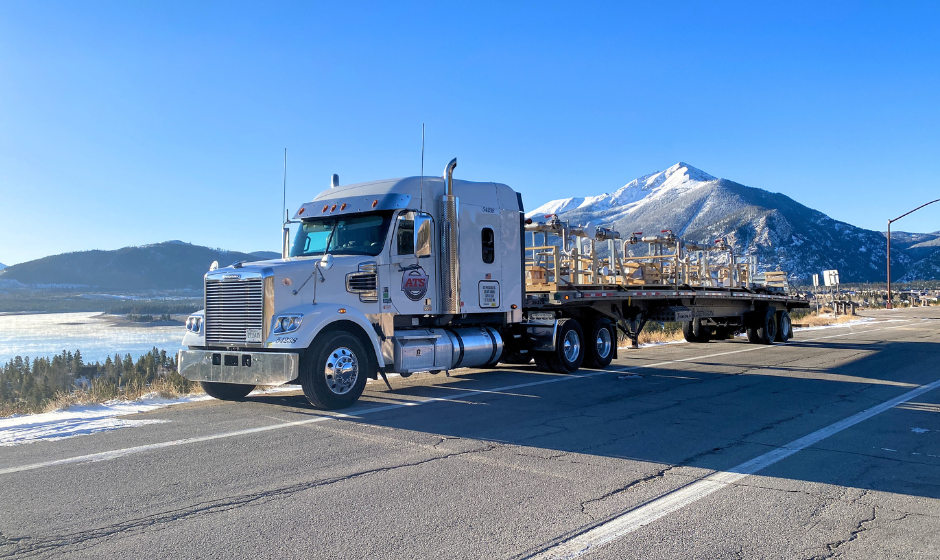 A semi truck with a flatbed trailer in a snowy mountain scene