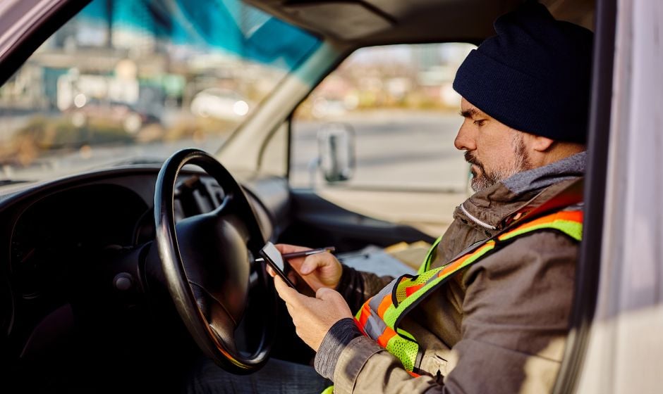 A parked trucker using a smartphone app to track freight