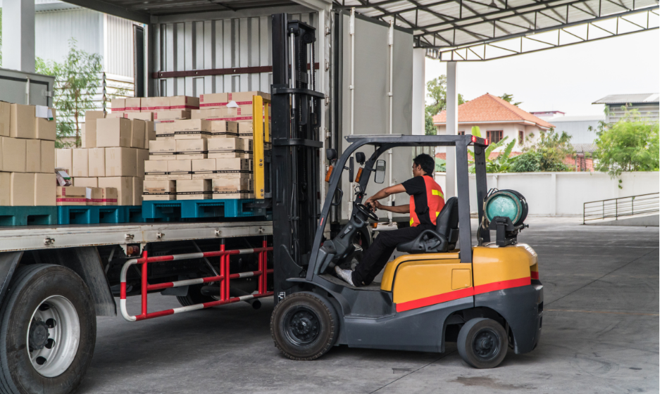 A worker uses a forklift to unload freight in a warehouse