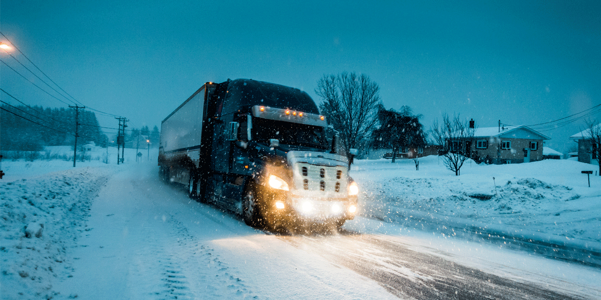 Semi-truck driving on a snowy road at dusk.