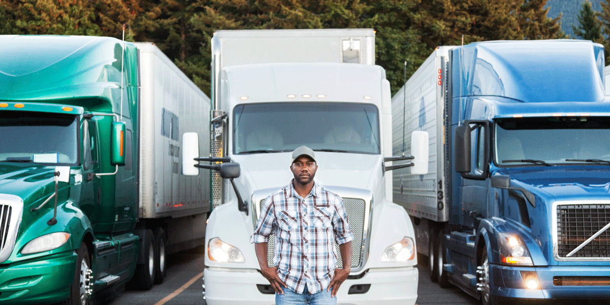 Truck driver standing in front of three semi-trucks.