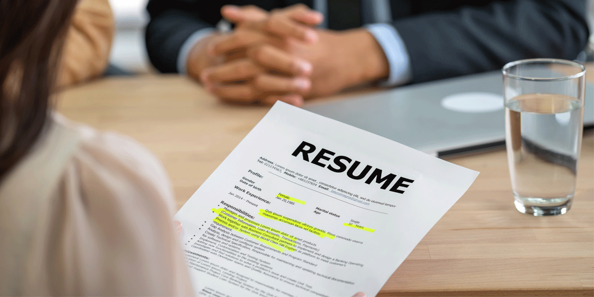 Woman holding resume during an interview. She sits across from a man with folded hands.