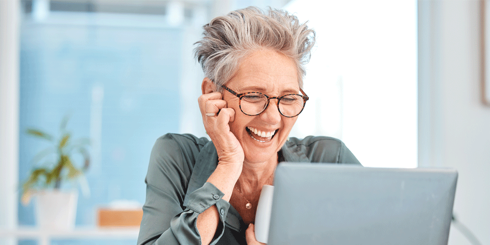 Woman with short gray hair looking at laptop and laughing.