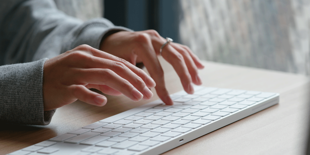 Woman typing on a wireless white keyboard.