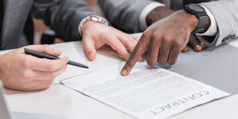 One man signing a contract while another points where to sign.