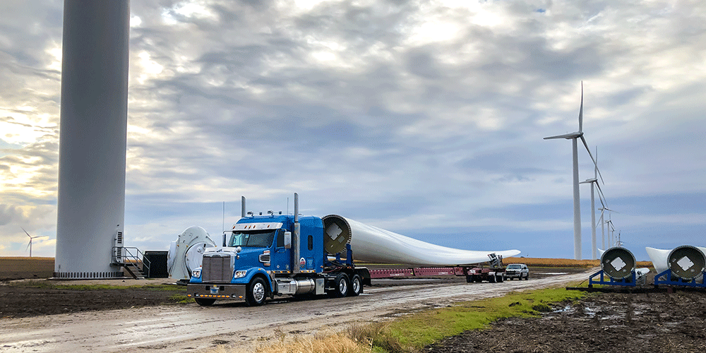 Blue semi tractor hauling wind blade at wind site