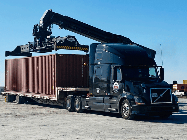 An ATS truck pulling a step-deck trailer is loaded with a cargo container.