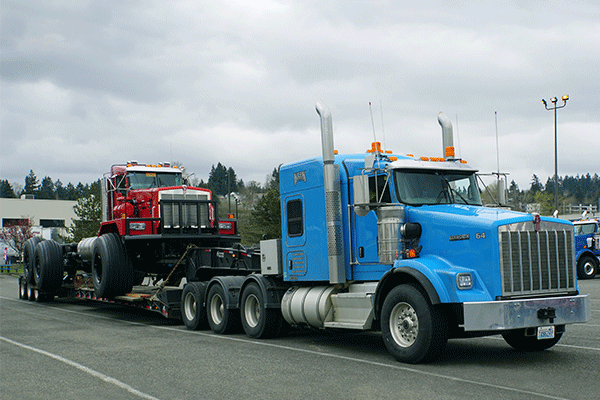 A bright blue truck pulls an open deck trailer carrying heavy machinery.
