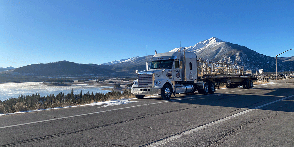 Flatbed truck and trailer parked on the side of the road in front of mountains