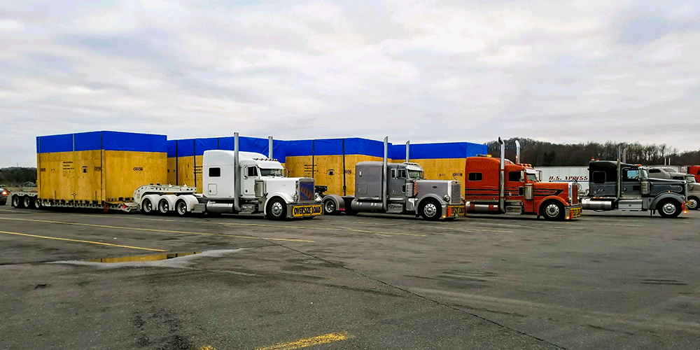 Four removable gooseneck tractor-trailers lined up in parking lot