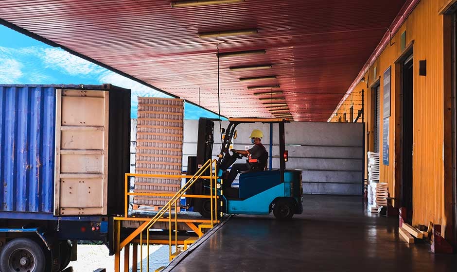 Blue shipping container being unloaded by forklift at warehouse