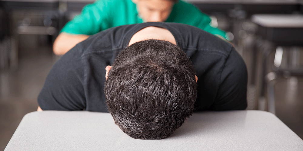 Student with head down on desk in classroom