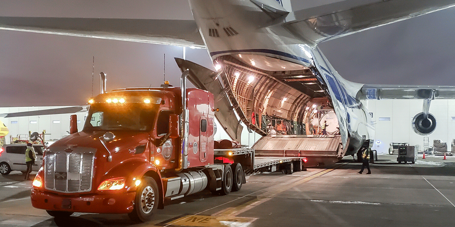 Semi truck with a step-deck trailer backed up to Antonov aircraft