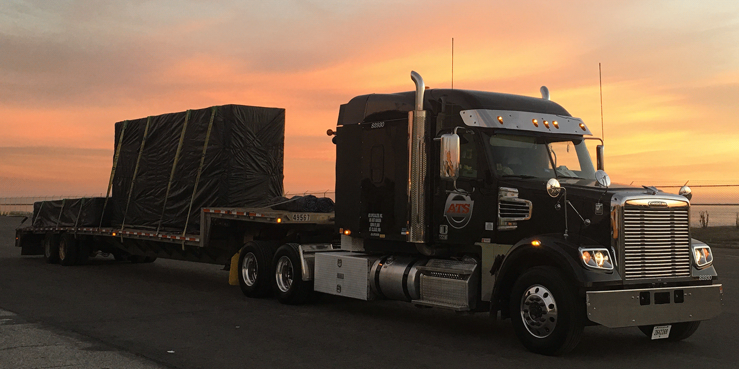 Black semi-tractor with step-deck trailer at sunset