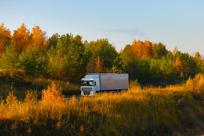 A semi truck pulling a dry van trailer travels on a highway in autumn
