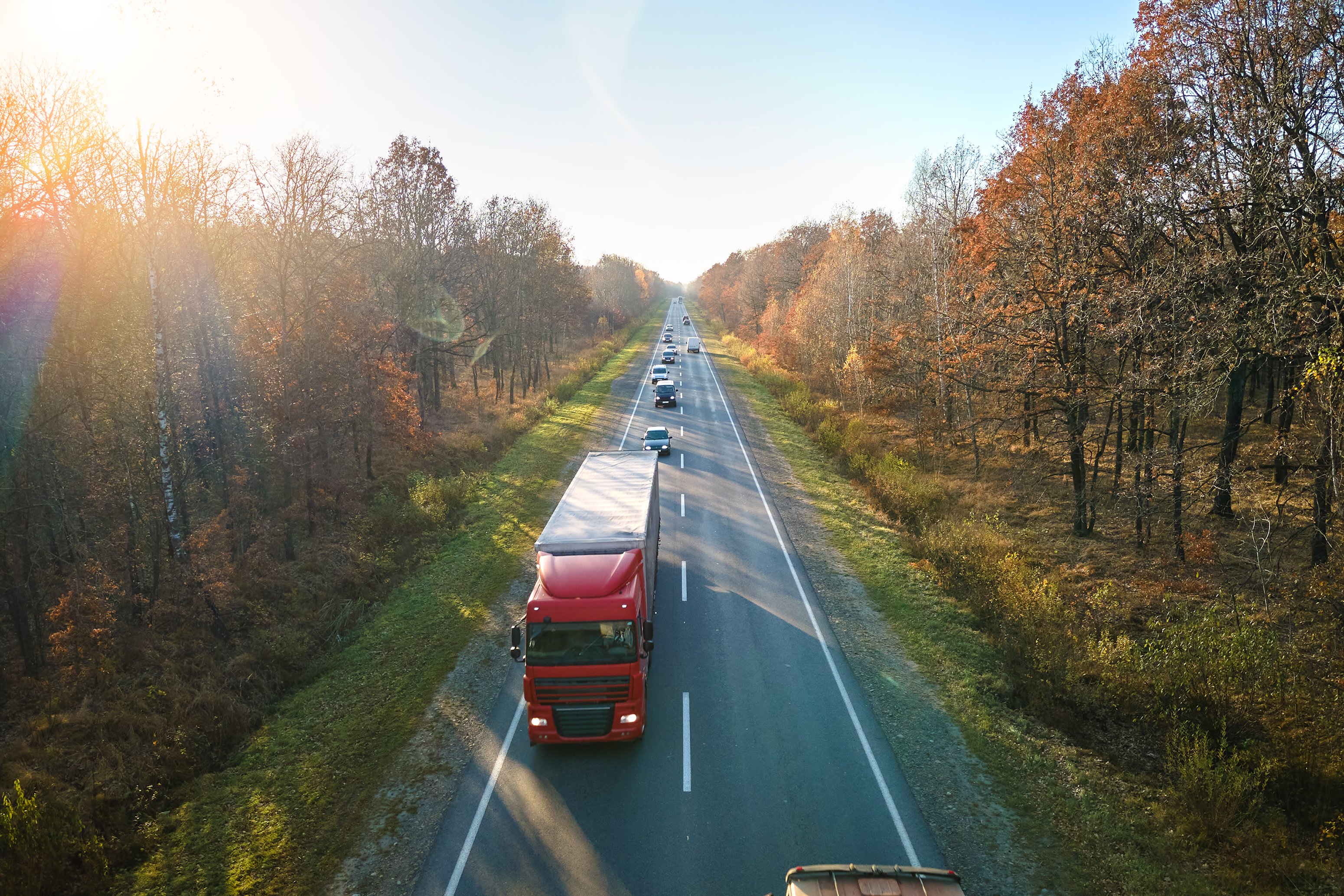 Aerial view of a semi truck traveling down a split-lane road in autumn
