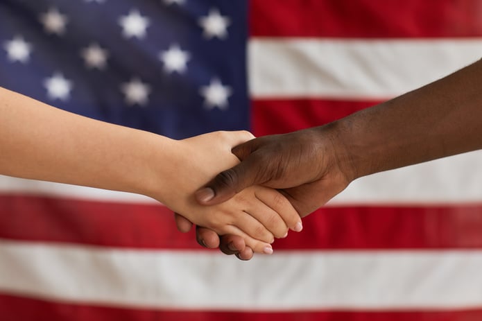Business people shaking hands against an American flag backdrop.