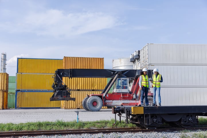 Workers stand on a rail car that will be loaded with freight containers