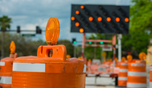 A street under construction, with a traffic cone in the foreground with a flashing arrow sign in the background.