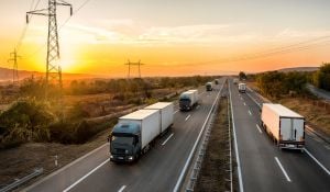 Several trucks and vehicles travel on a midwestern road at sunset