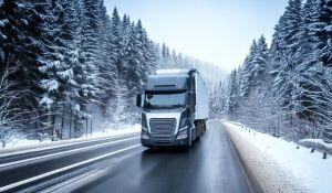 A semi truck and dry van trailer travel down a road in snowy winter weather