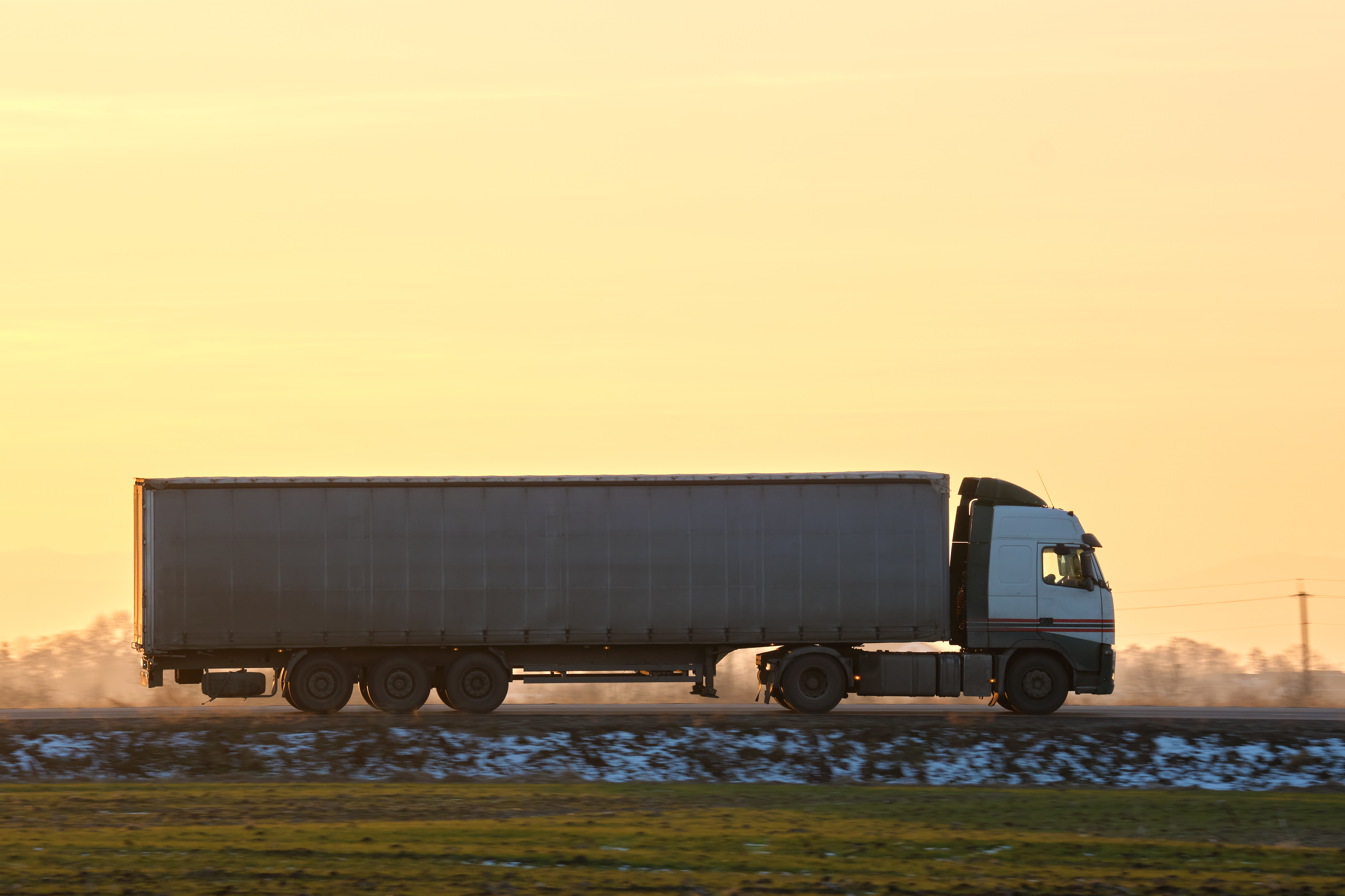 A semi truck with trailer travels on a road in the early spring